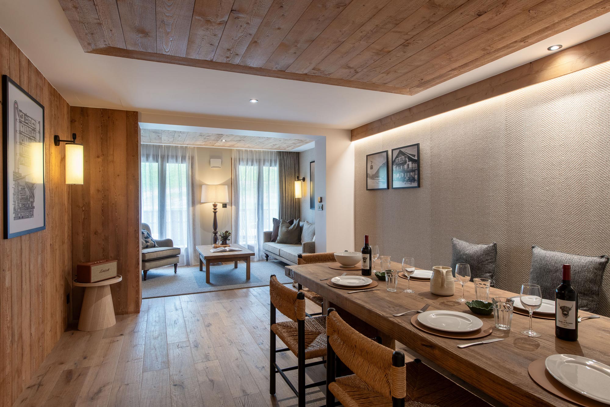 Wooden dining table and living area with large windows beyond in Apartment Abeille, Morzine
