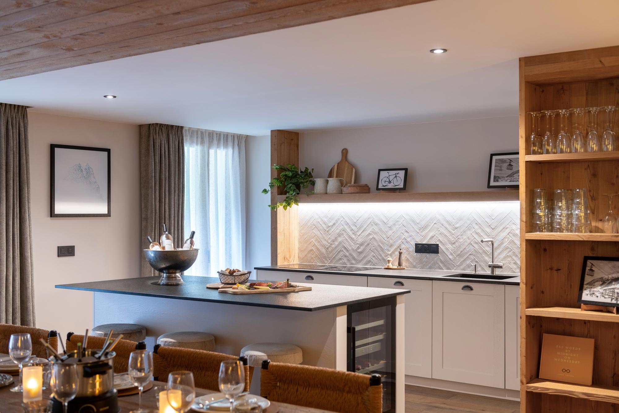 Kitchen island and dining table set with candles and glassware, with herringbone splashback and open shelving in Apartment Chamossière, Morzine