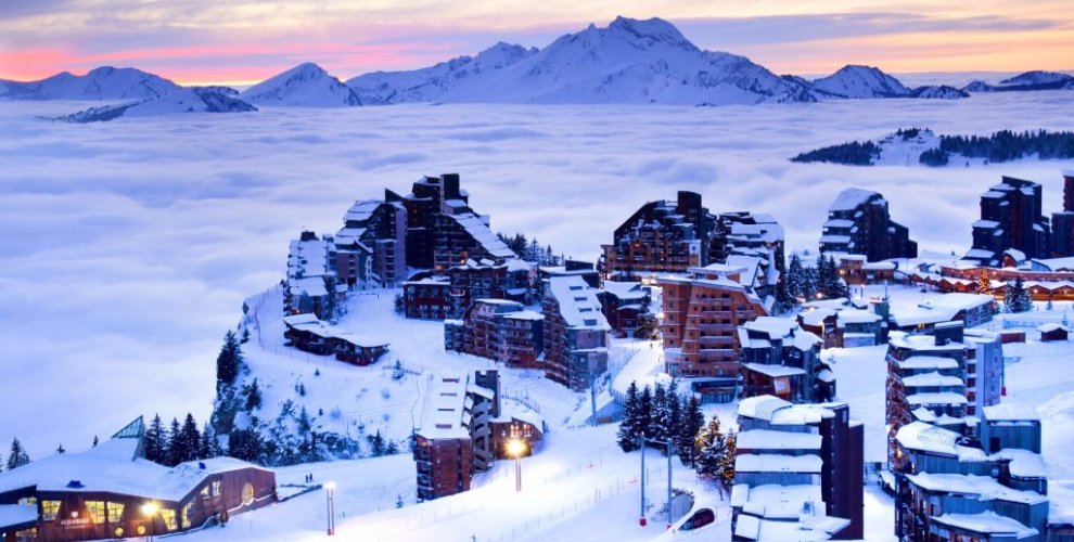Snow-covered Avoriaz 1800 chalets glowing at sunset above a sea of cloud, with pink skies and distant peaks
