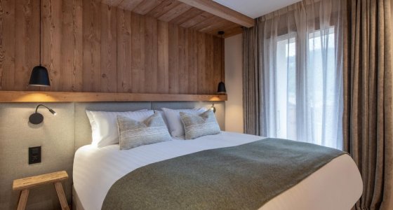 Double bedroom with olive-green throw and tall curtained windows in Apartment Abeille, Morzine
