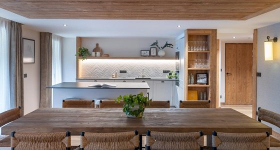 Wooden dining table surrounded by chairs with kitchen beyond in Apartment Chamossière, Morzine