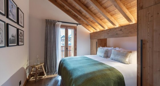 Bedroom with sloping beams, green bed runner and tall window in Apartment Le Stade, Morzine