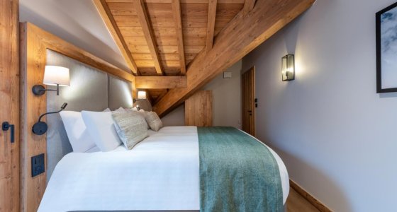 Bedroom under a sloping timber ceiling with green bed runner in Apartment Chamossière, Morzine