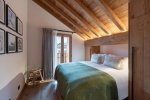 Bedroom with sloping beams, green bed runner and tall window in Apartment Le Stade, Morzine