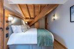 Bedroom under a sloping timber ceiling with green bed runner in Apartment Chamossière, Morzine